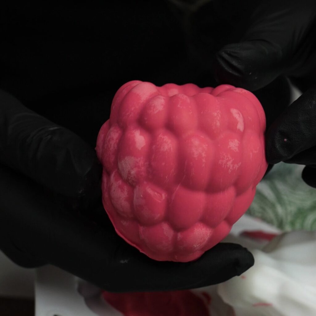 Hands holding chocolate raspberry yogurt gem just removed from mould