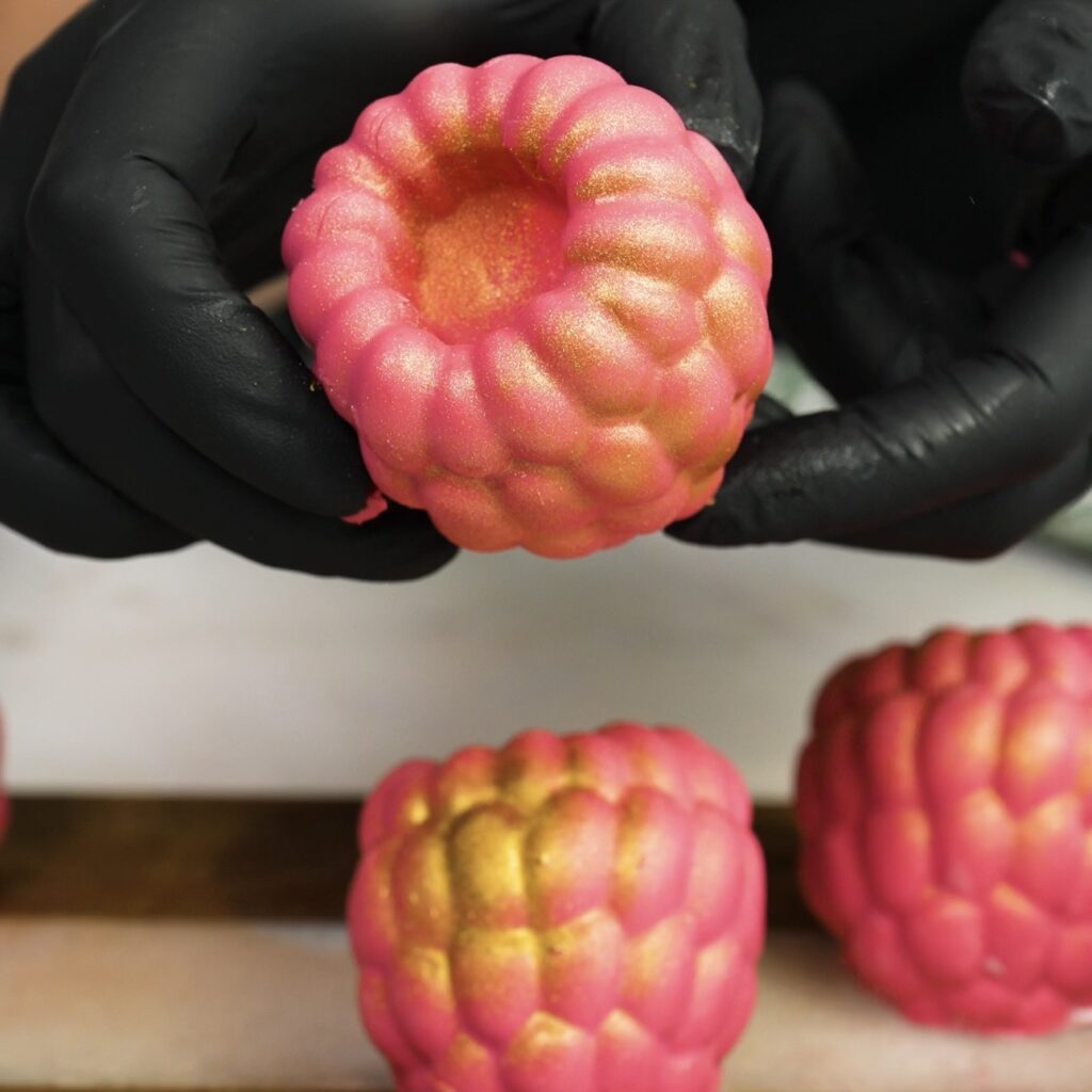 Hands holding chocolate raspberry yogurt gem dusted with edible gold