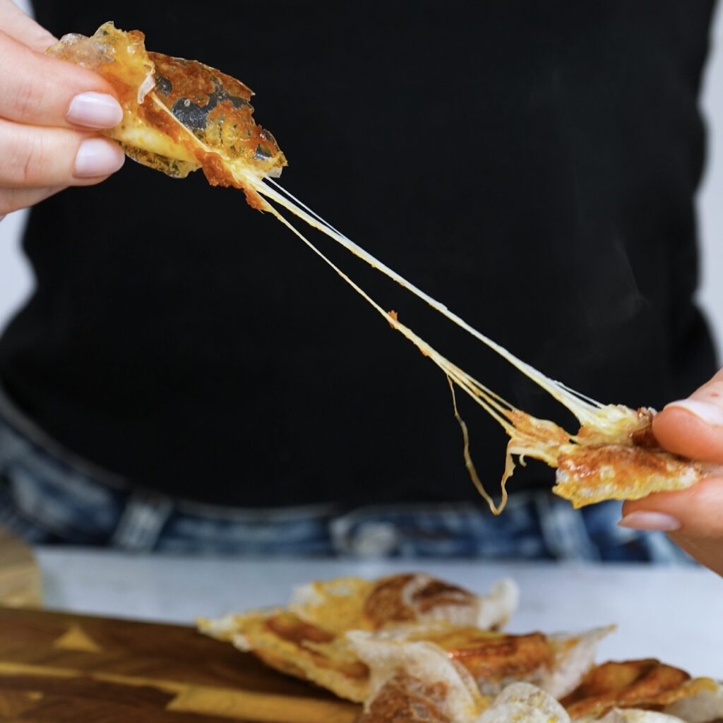 Hands pulling apart a crispy rice paper chip with gooey mozzarella