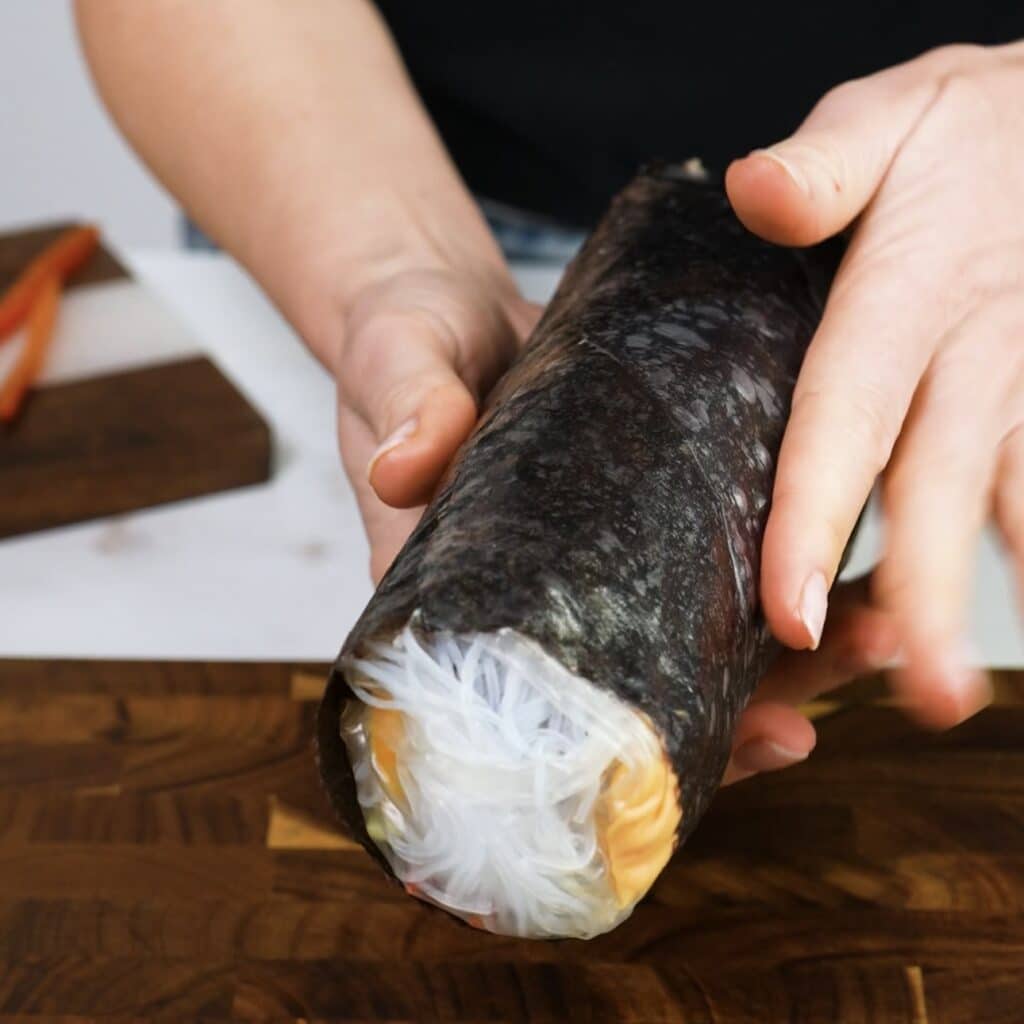 Hands holding a freshly rolled rice paper chicken nori roll