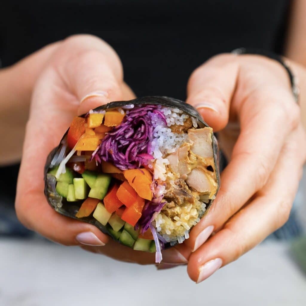 Hands holding a sliced piece of rice paper chicken nori roll showing the filling