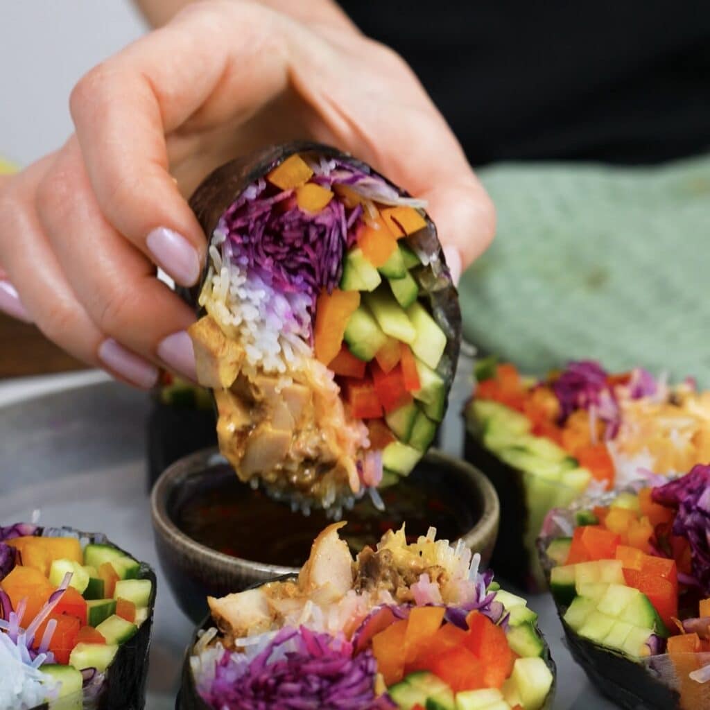 Dipping a rice paper chicken nori roll into dipping sauce