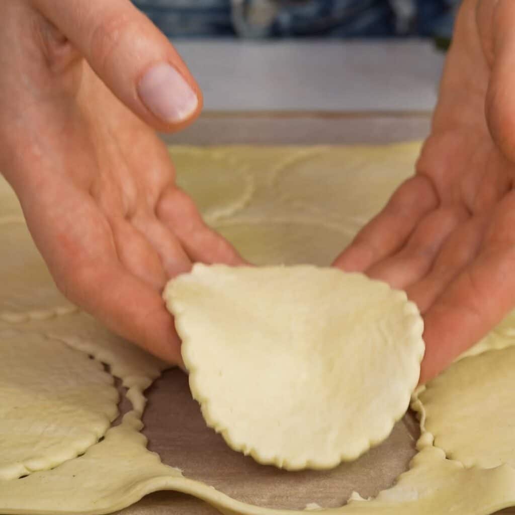 Hands holding a cut puff pastry circle ready for shaping
