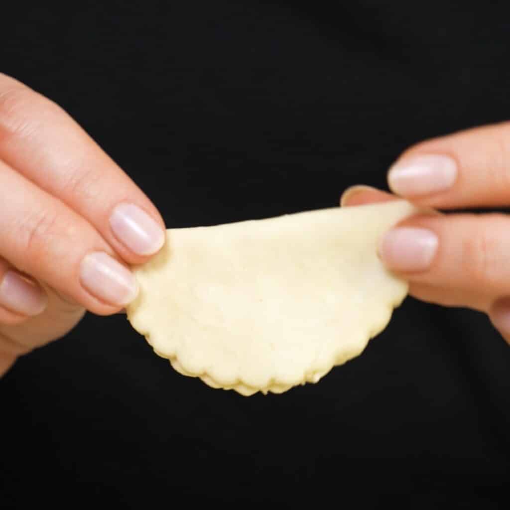 Hands holding a folded puff pastry semicircle ready for baking