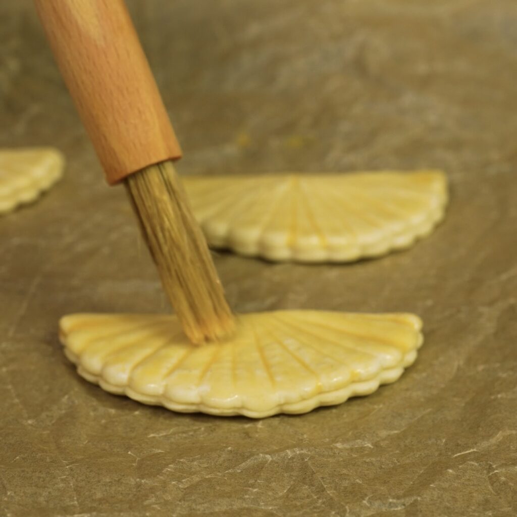 Brushing puff pastry semicircles with egg wash before baking