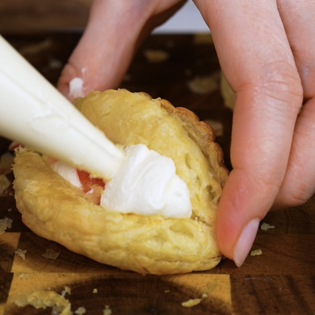 Piping cream cheese filling into puff pastry shells