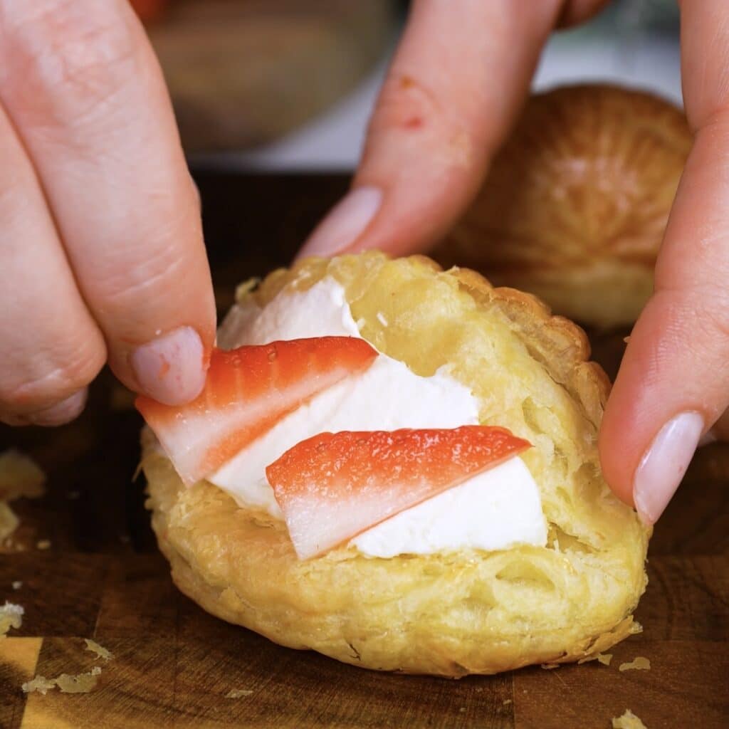 Decorating puff pastry shells with fresh strawberry slices