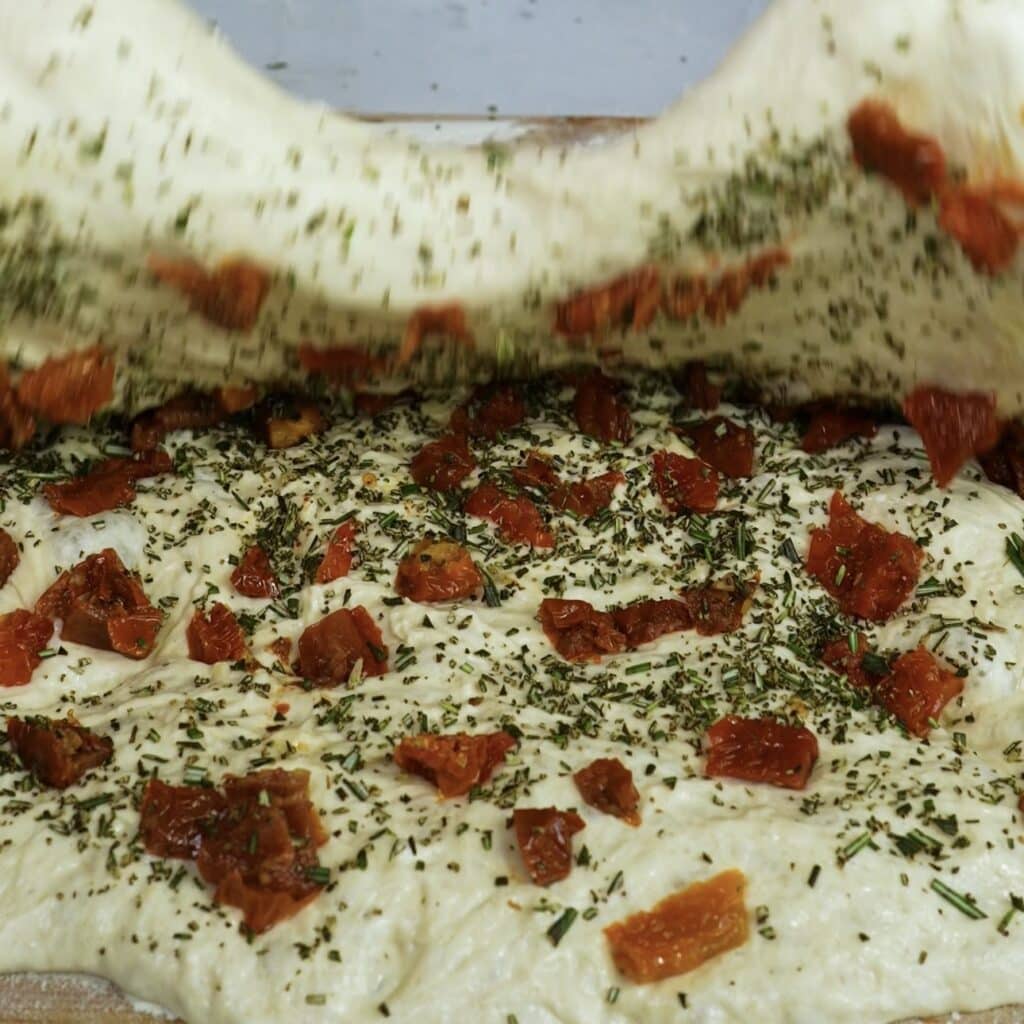 Folding dough over sun-dried tomatoes and rosemary filling