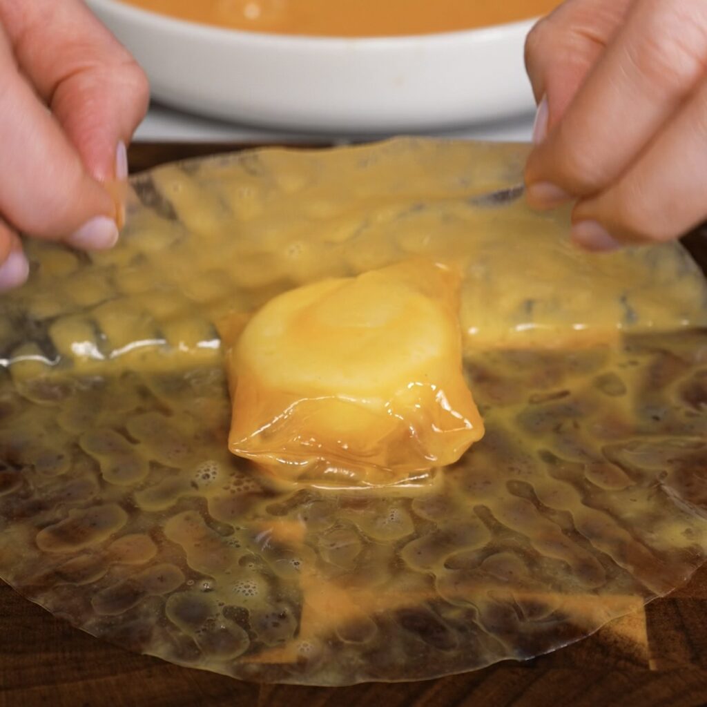First-wrapped Babybel cheese placed on egg-dipped rice paper for second wrap