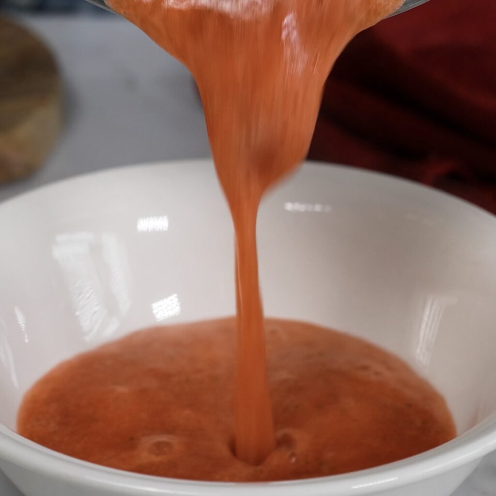 Pouring homemade strawberry syrup into a bowl for dipping sponge fingers