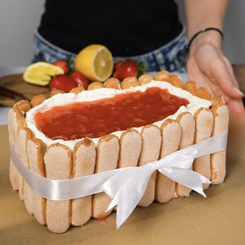 Piping remaining strawberry sauce and tying ribbon around tiramisu