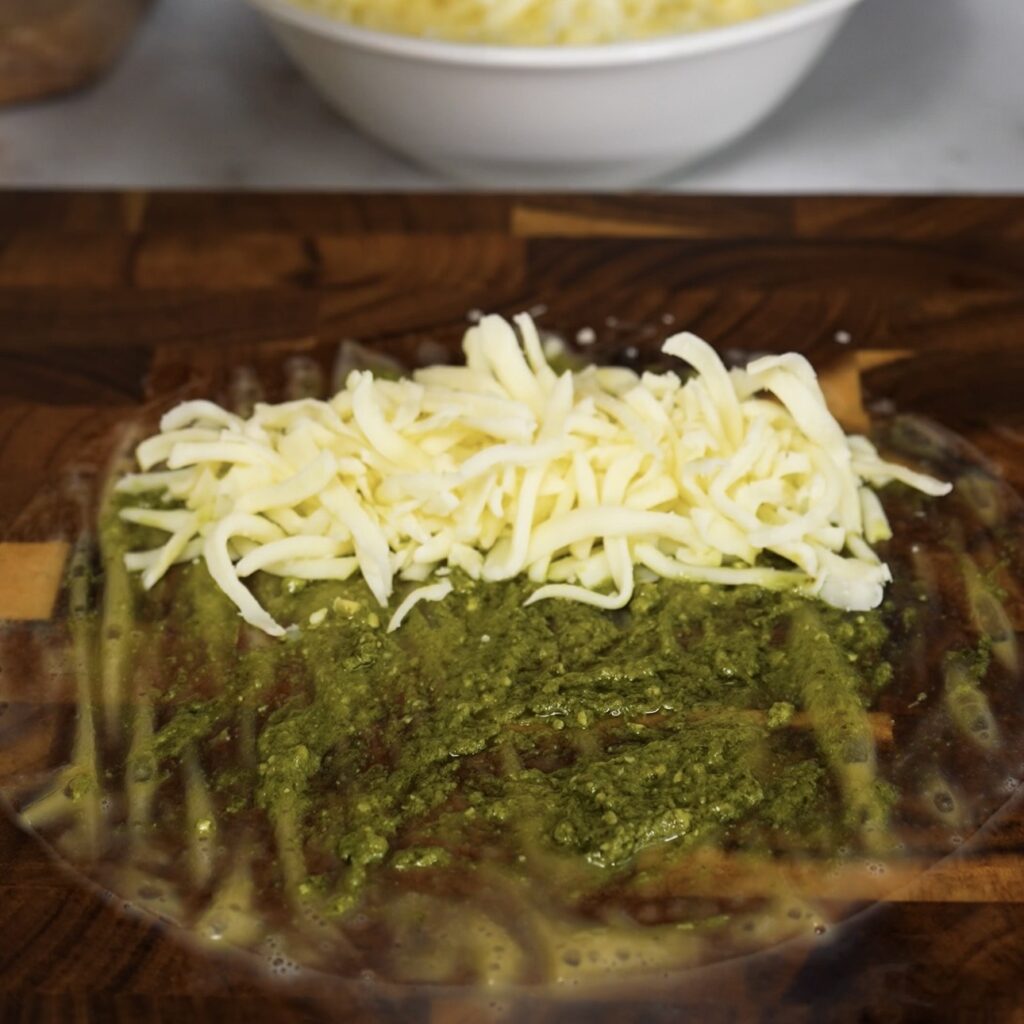 Rice paper sheet topped with pesto and grated mozzarella before rolling