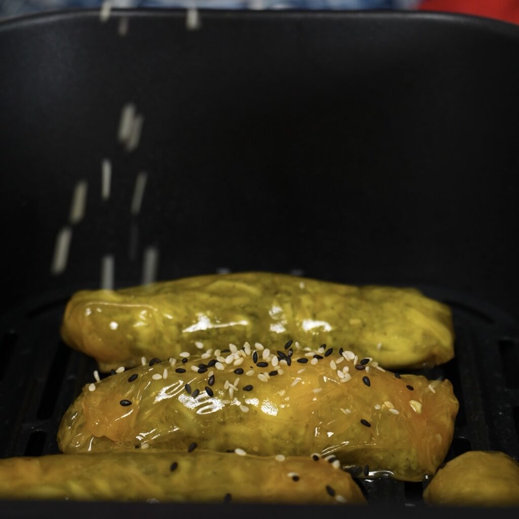 Rice paper sticks in air fryer basket sprinkled with sesame seeds before cooking