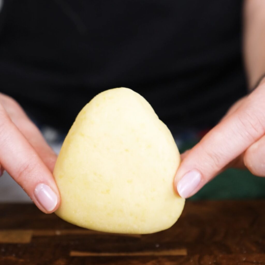 Hands holding a shaped potato triangle ready for coating
