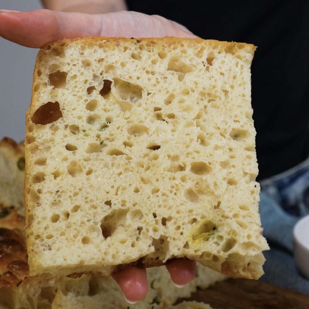 Slice of focaccia showing soft airy crumb with open holes and golden crust