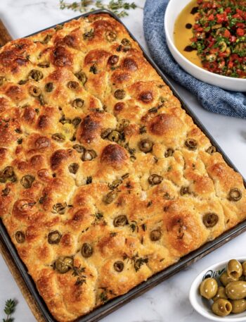 Freshly baked focaccia in a baking tray with golden crust, olives, and thyme