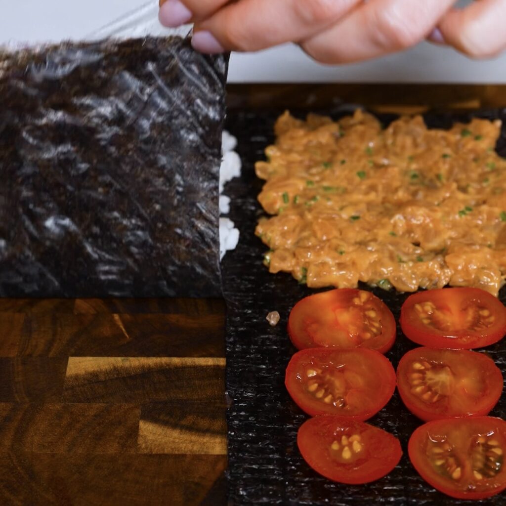 Folding the nori and rice paper layer over the sushi rice while shaping salmon sushi parcels