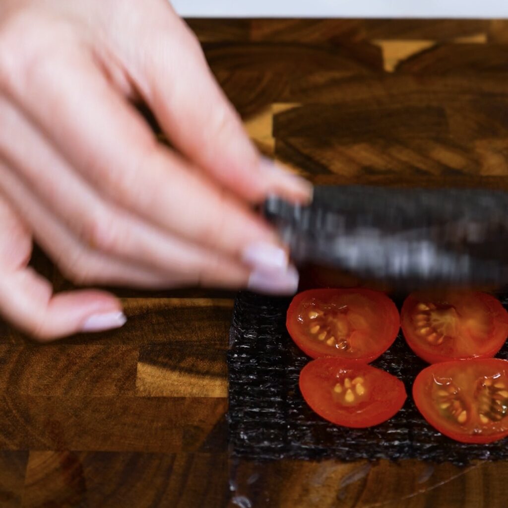 Folding the layered salmon sushi parcel over the tomato section during assembly