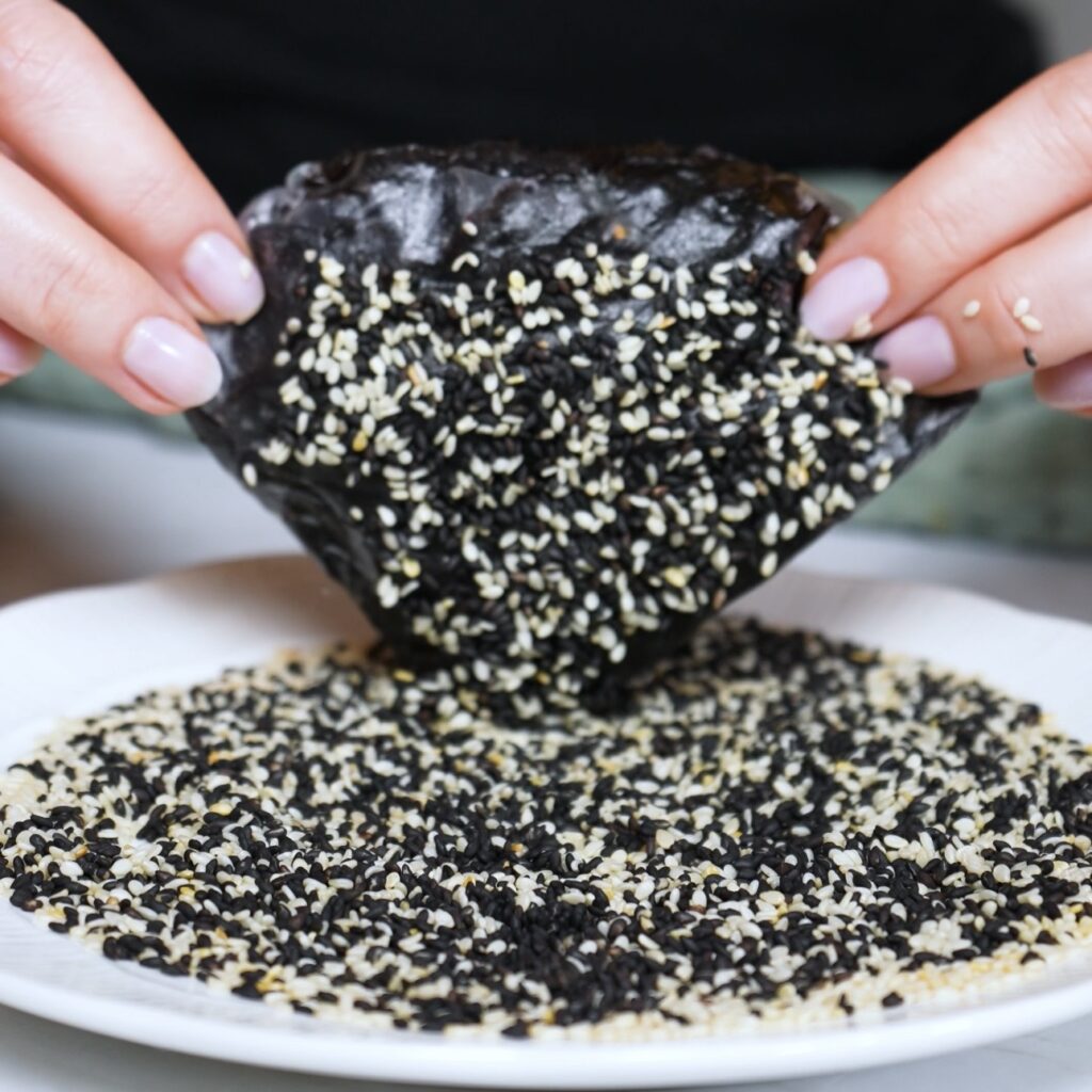 Dipping the salmon sushi parcel into black and white sesame seeds before air frying
