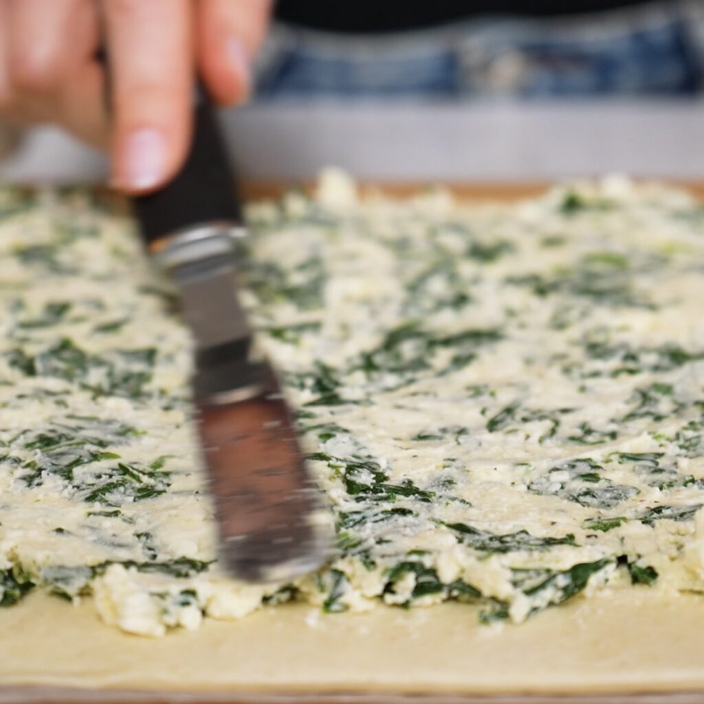Spreading spinach and feta filling over puff pastry before rolling