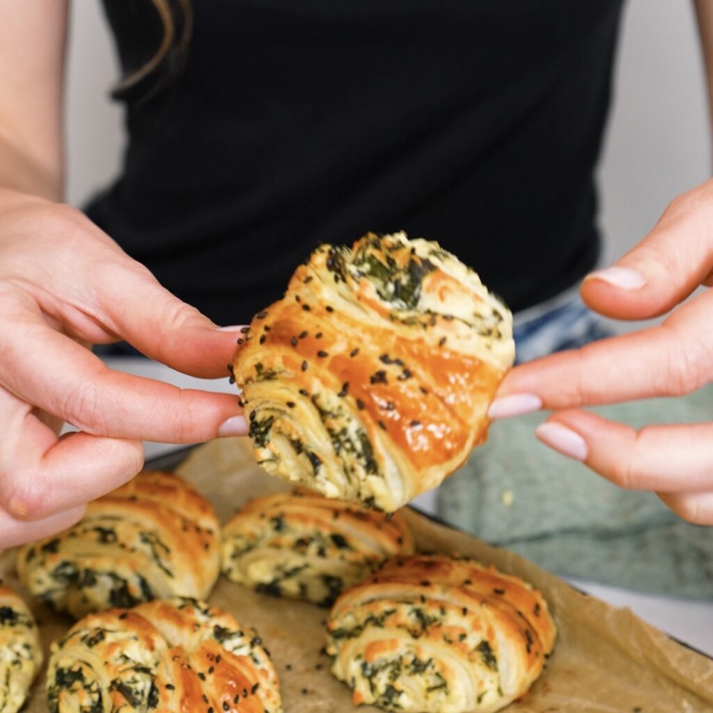 Hands holding a freshly baked spinach and feta puff pastry roll
