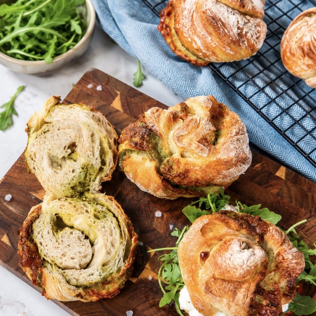 Freshly baked No-Knead Pesto Mozzarella Bread Twists served on a wooden board with one piece sliced open to show the soft interior.