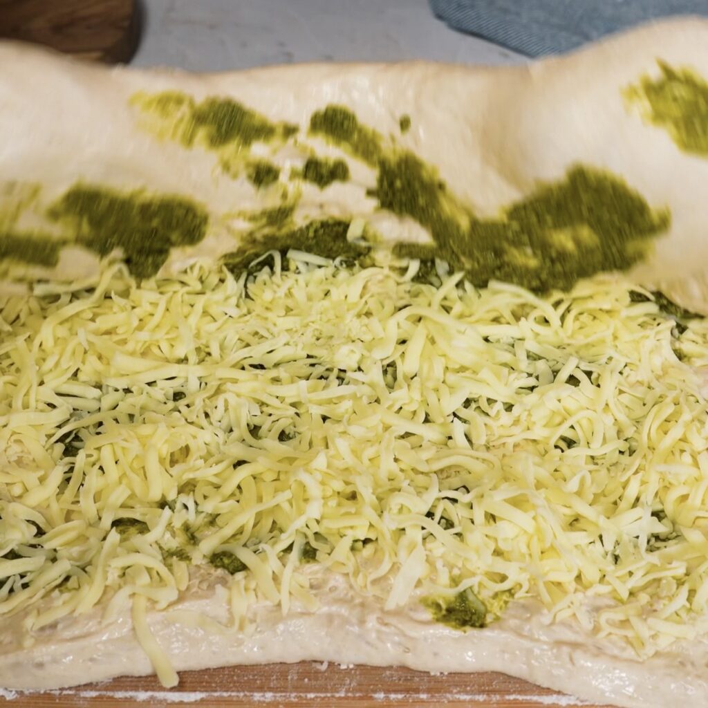 Dough folded over pesto and mozzarella filling on a floured work surface.