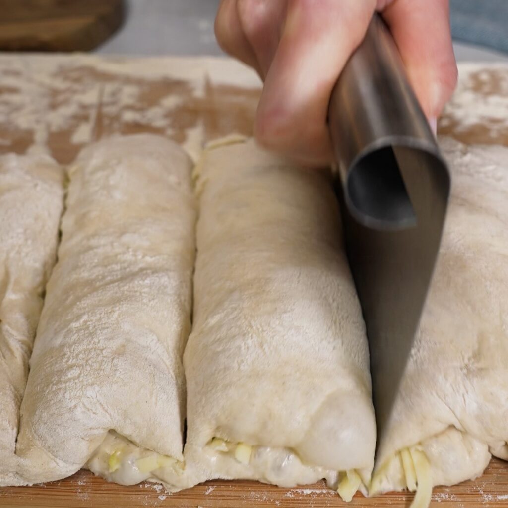 Filled pesto mozzarella dough cut into six equal pieces on a floured work surface.