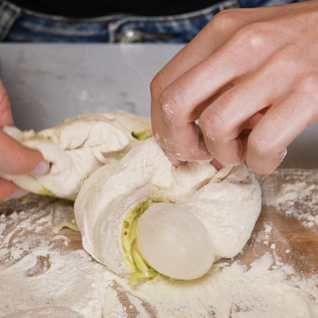 Twisted pesto mozzarella dough strip rolled into a bun shape on a floured work surface.