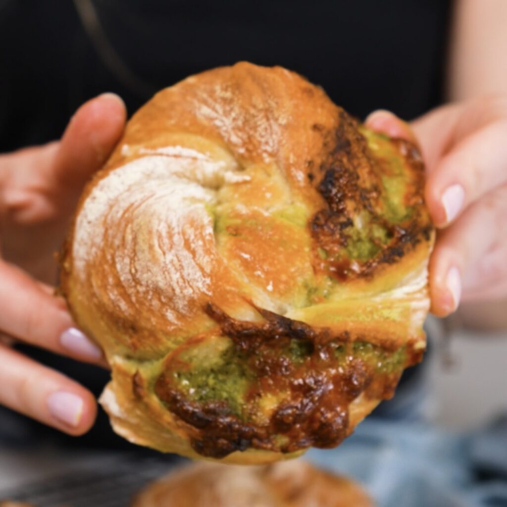 Hands holding freshly baked No-Knead Pesto Mozzarella Bread Twists with golden crust and cheesy pesto layers.