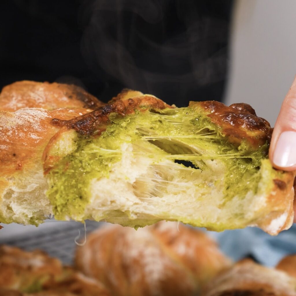 Hands tear open a baked bread twist to show the mozzarella pull and soft airy interior.