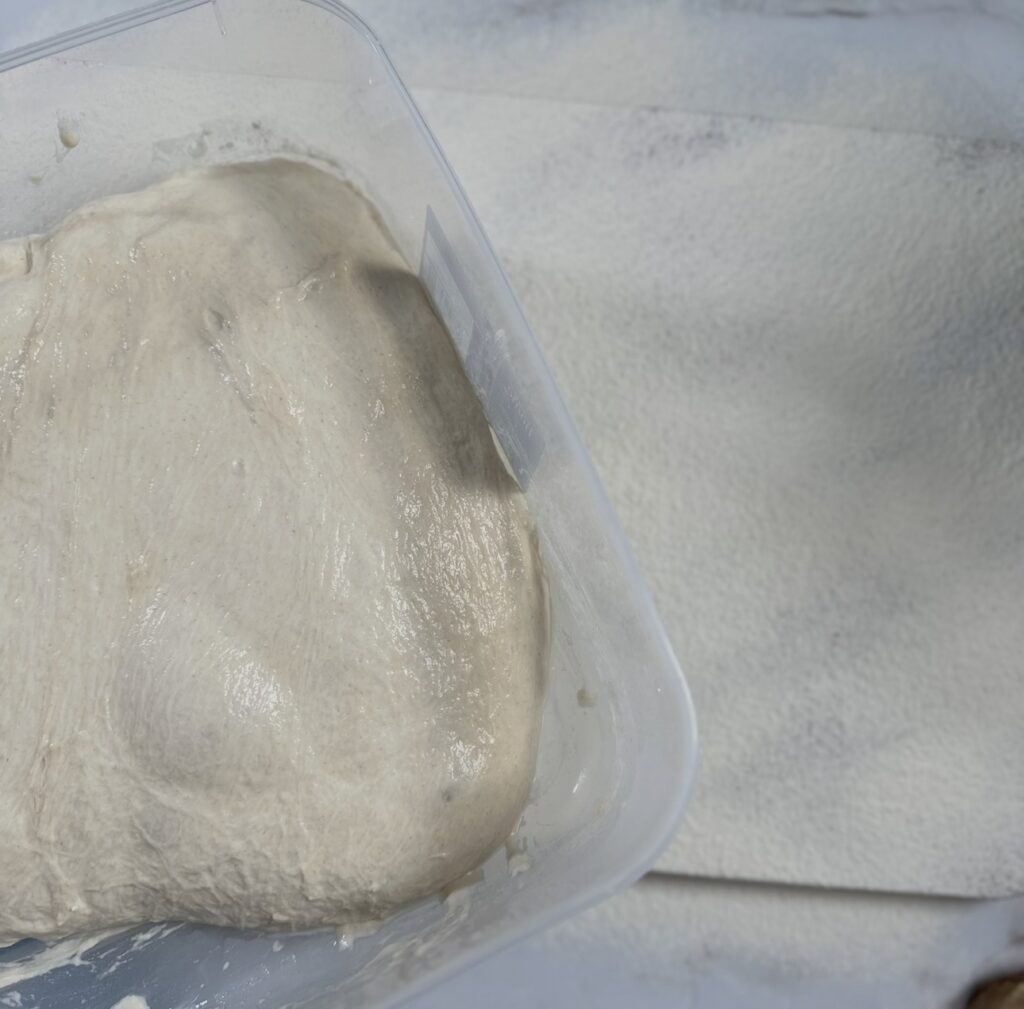 No-knead bread dough rests in a container after an overnight chill, with a floured work surface ready for shaping.
