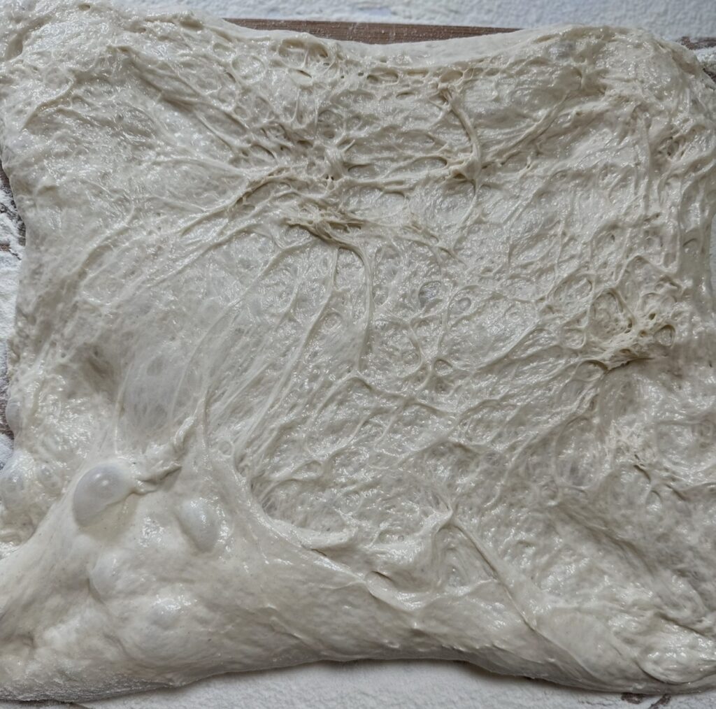 No-knead bread dough stretched and tidied into a square shape on a floured work surface.