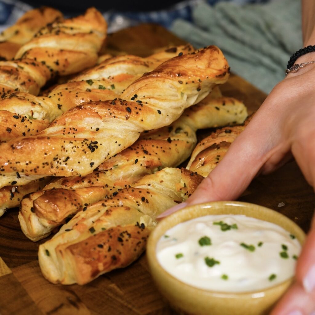 Smoked salmon puff pastry twists served on a wooden board with garlic yoghurt sauce.