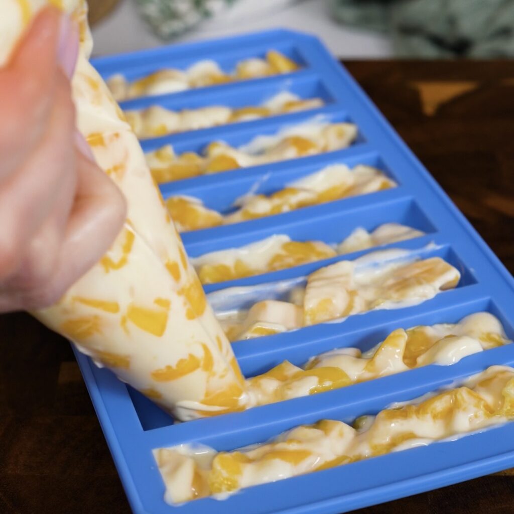 Piping mango yogurt mixture into an ice stick mould.