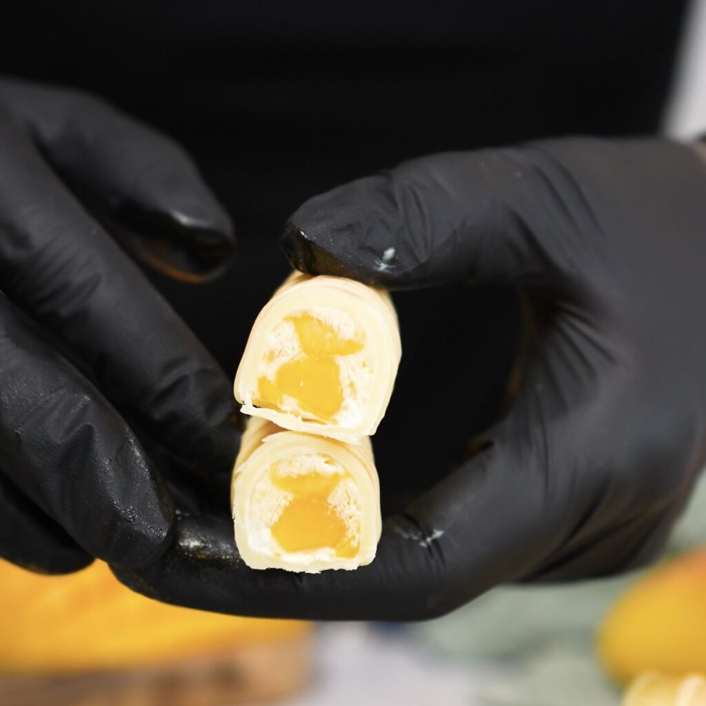 Hands holding a frozen mango yogurt bar cut in half to show the interior.