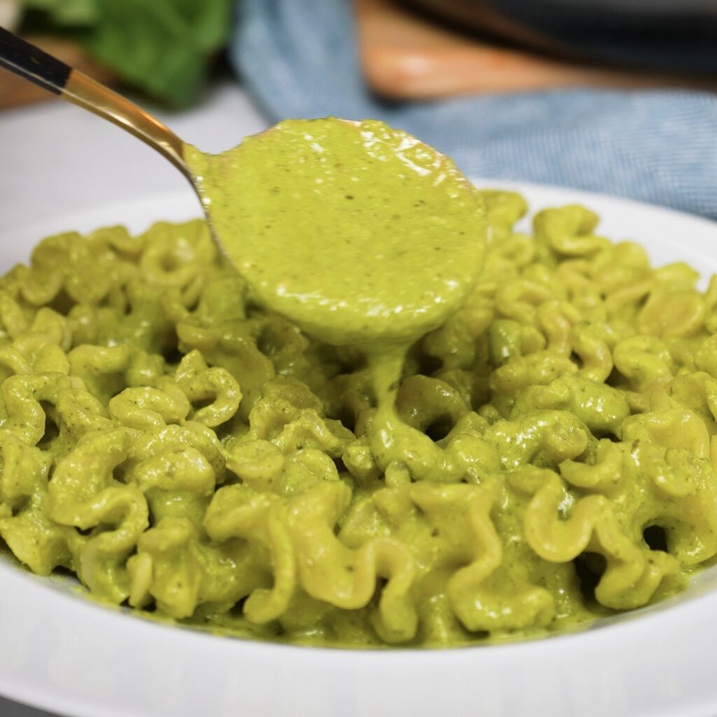 Pasta on a plate with creamy cottage cheese pesto sauce being poured over the top