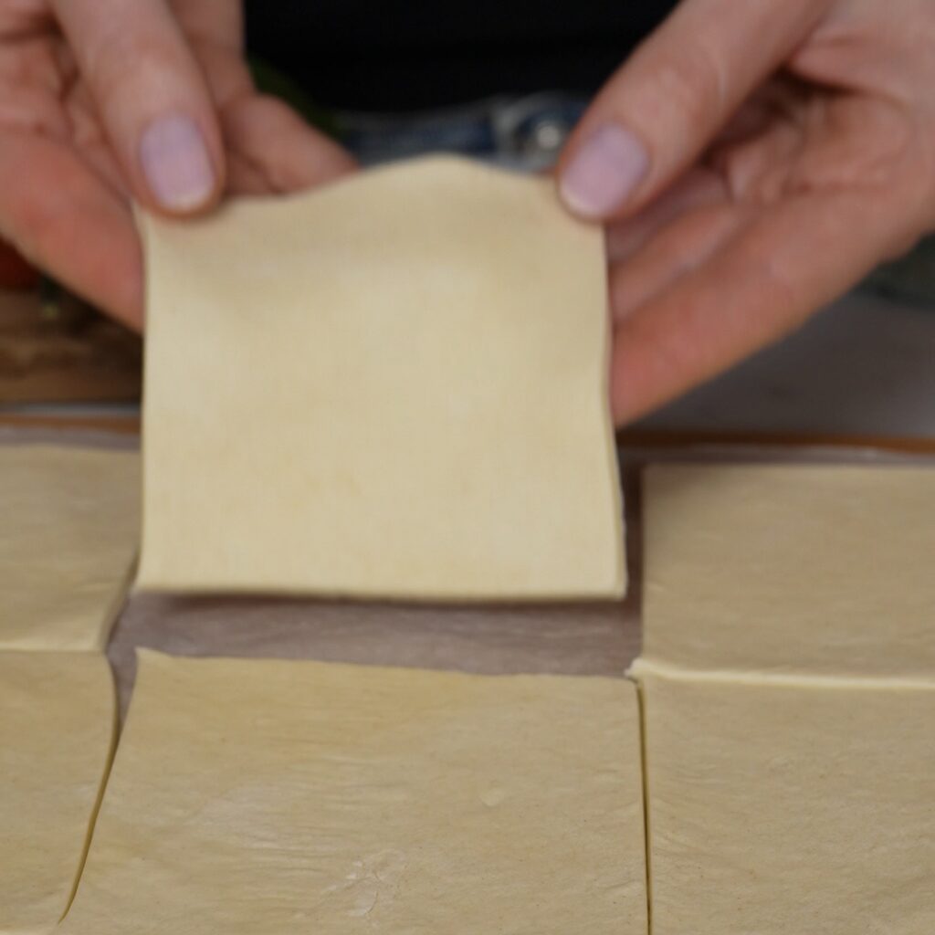 Puff pastry sheet cut into twelve equal squares for balsamic tomato and feta puffs.