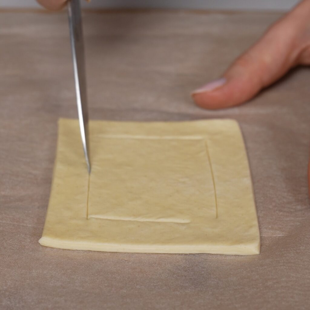 wo L-shaped cuts being made in one puff pastry square for balsamic tomato and feta puffs.