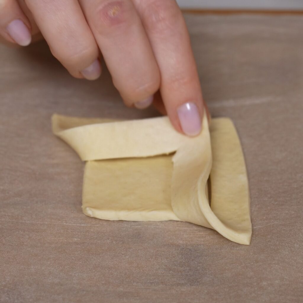 Loose puff pastry corner folded diagonally over the inner square to shape the tomato and feta puff.