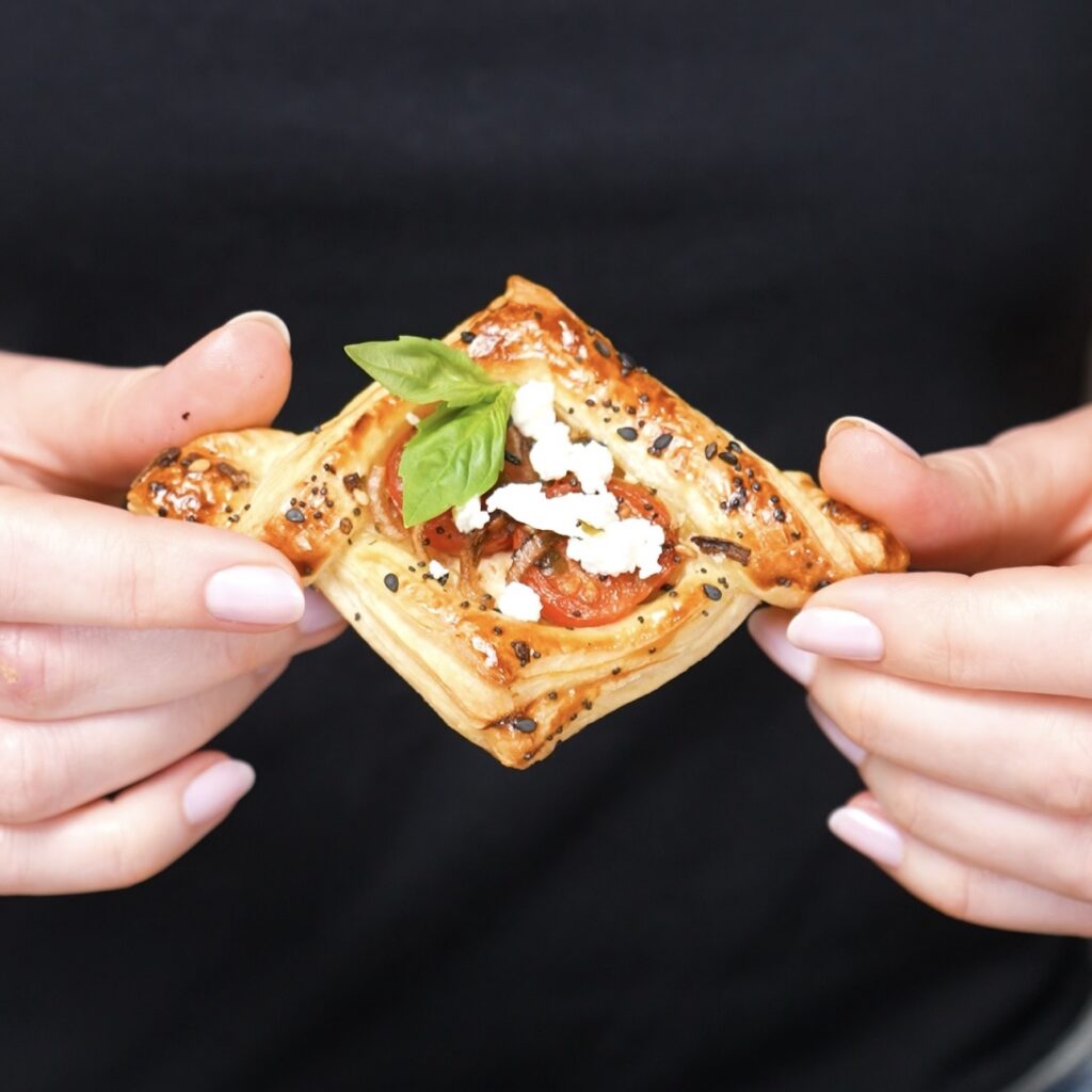 Hands holding a baked balsamic tomato and feta puff.