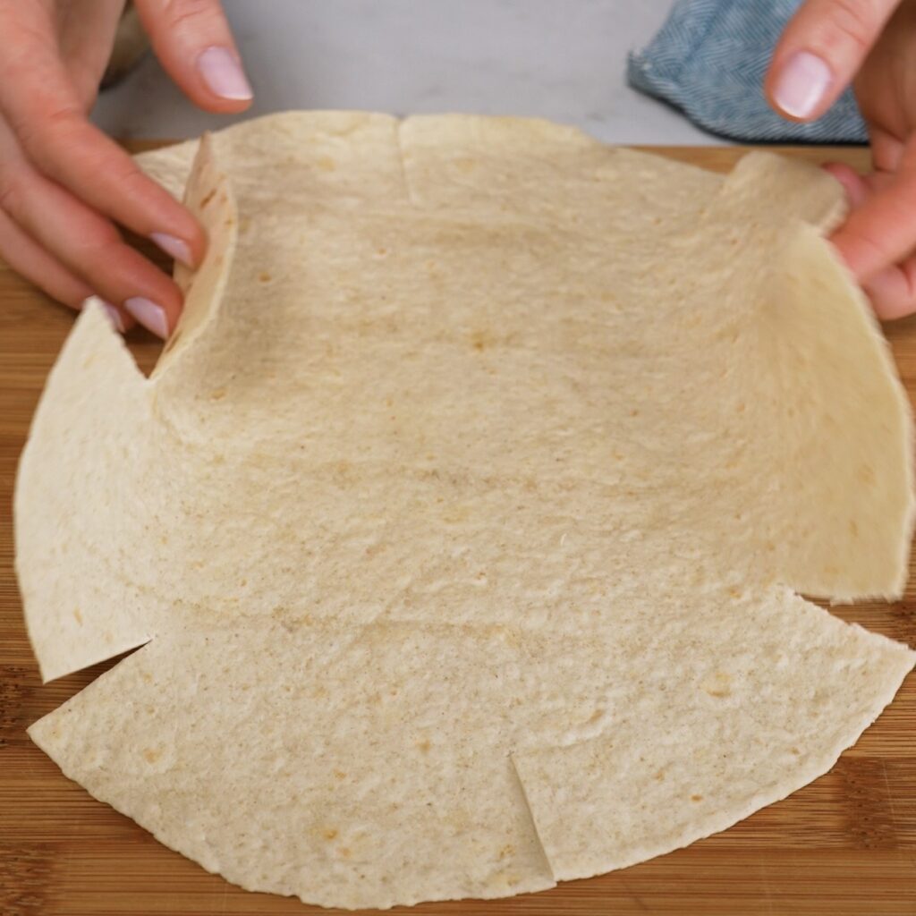 Tortilla with eight small cuts around the edge for shaping a quiche crust.
