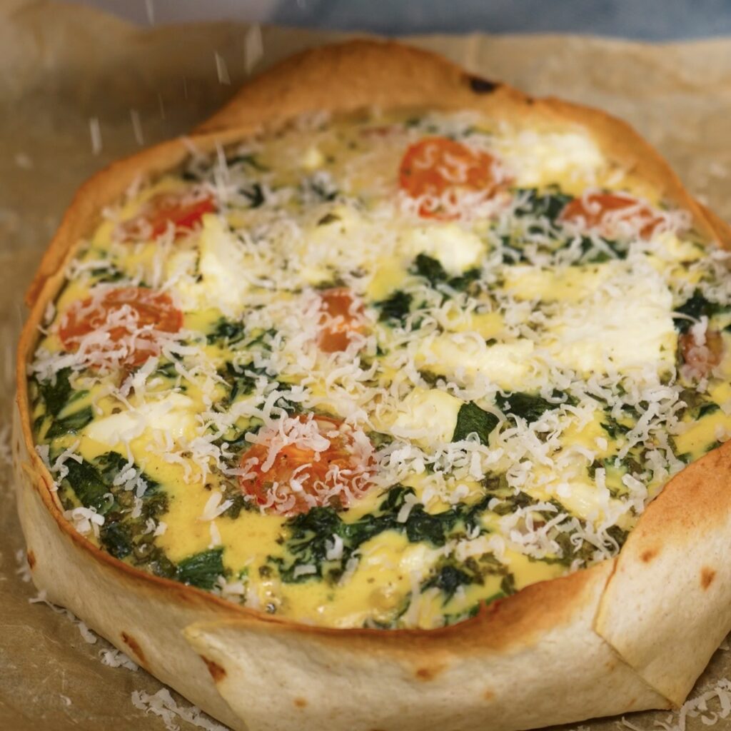Sprinkling grated Parmesan over the baked tortilla chicken quiche.