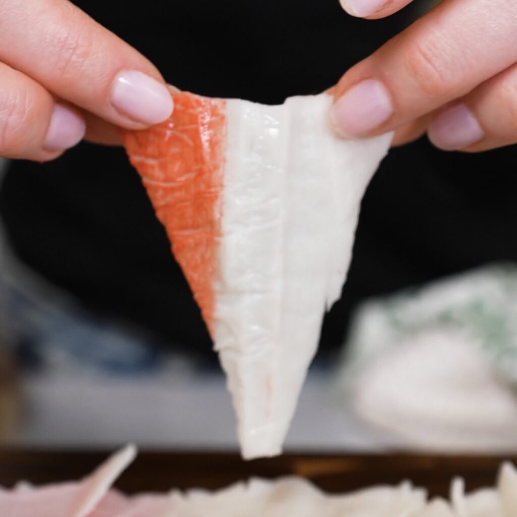 Hand holding a triangle-shaped crab stick chip before air frying.