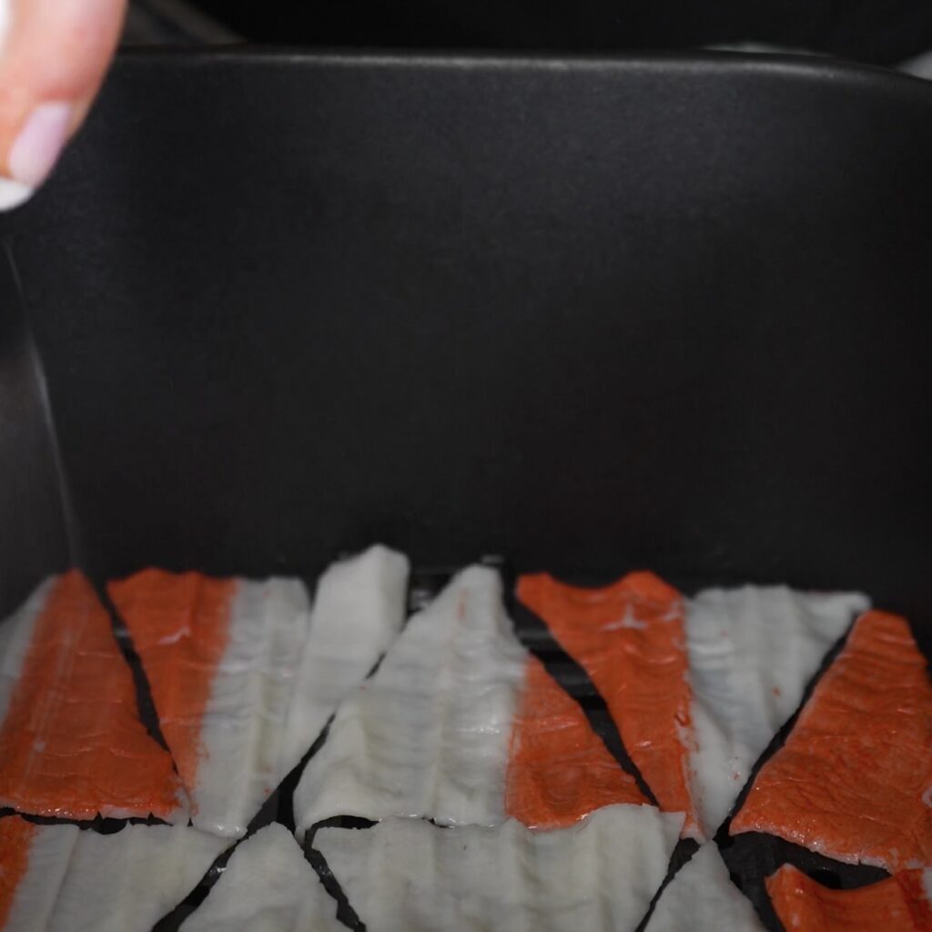 Crab stick chips arranged in an air fryer basket before cooking.