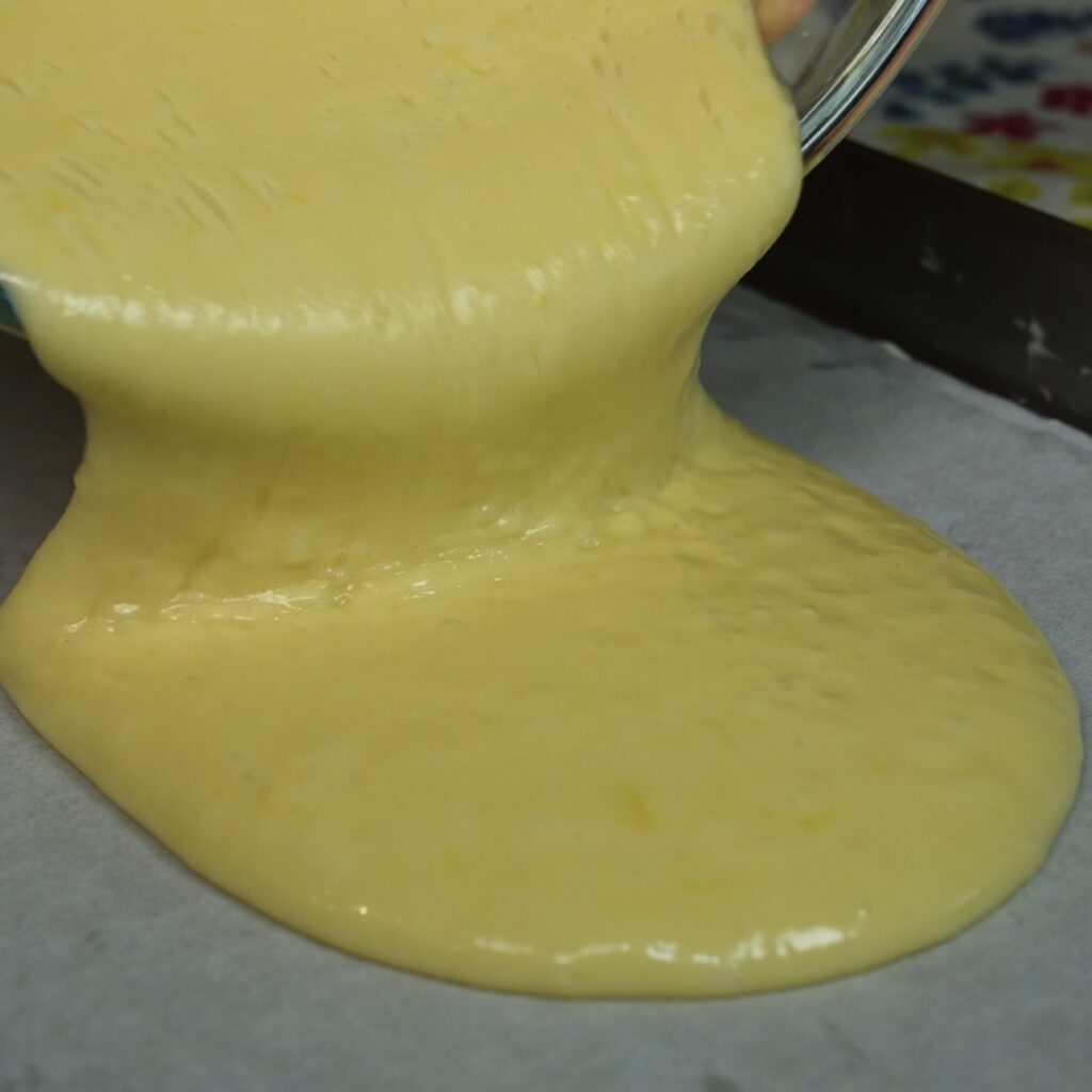 Pouring cake batter into a lined baking tray.