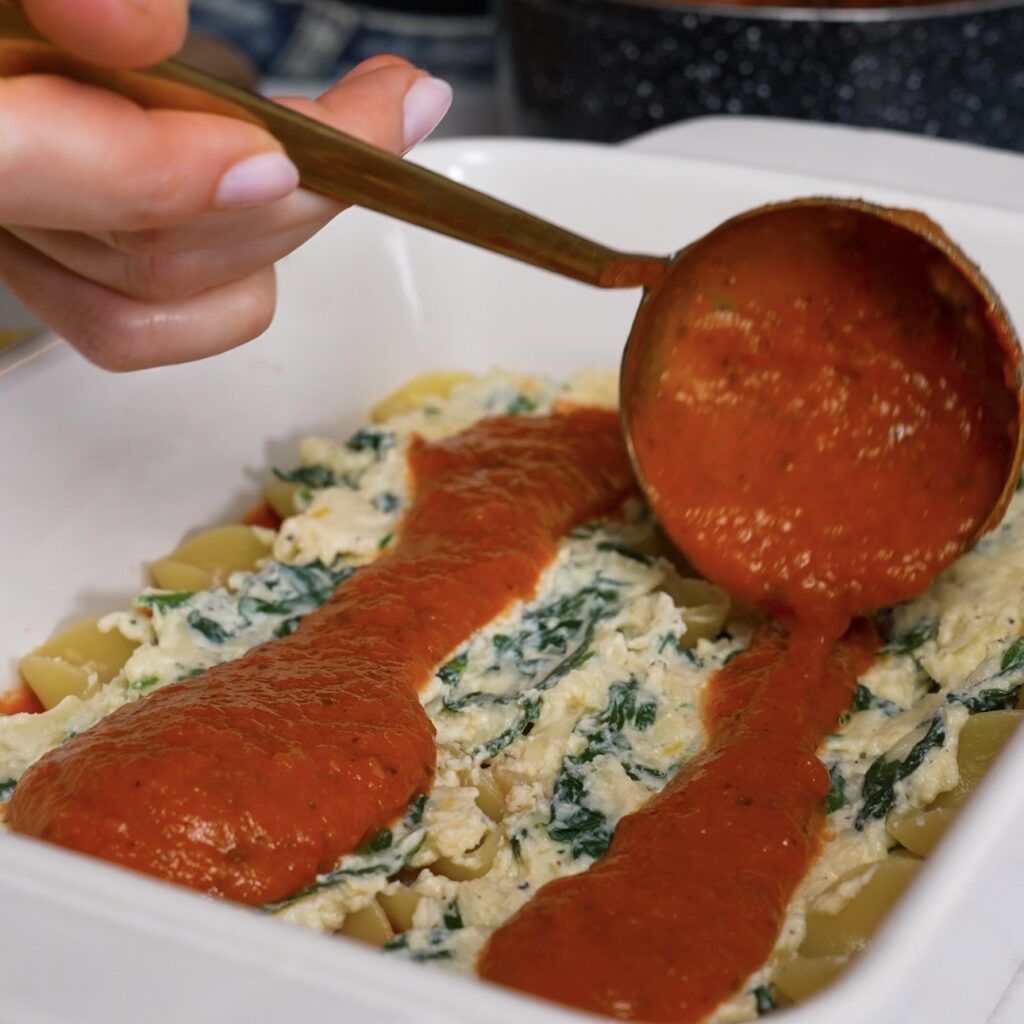 Adding marinara sauce over lasagna sheets and spinach ricotta filling