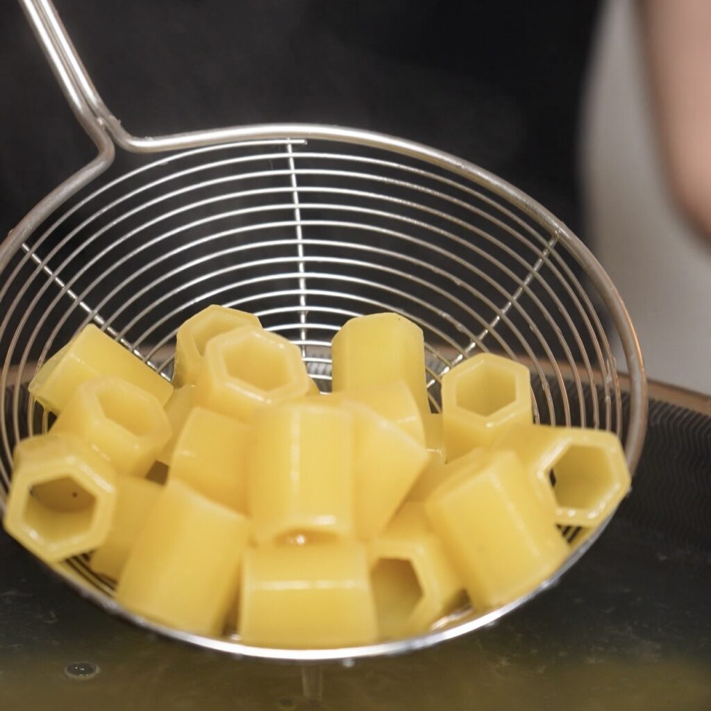Cooked short pasta being lifted from boiling water with a slotted spoon.