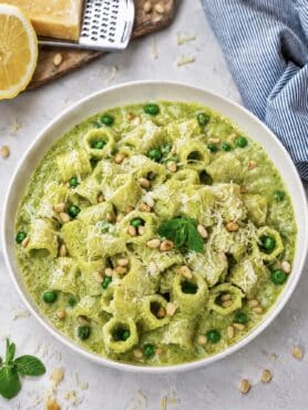High-protein pea and mint pasta served on a plate with Parmesan, peas, toasted pine nuts and mint.