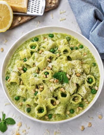 High-protein pea and mint pasta served on a plate with Parmesan, peas, toasted pine nuts and mint.